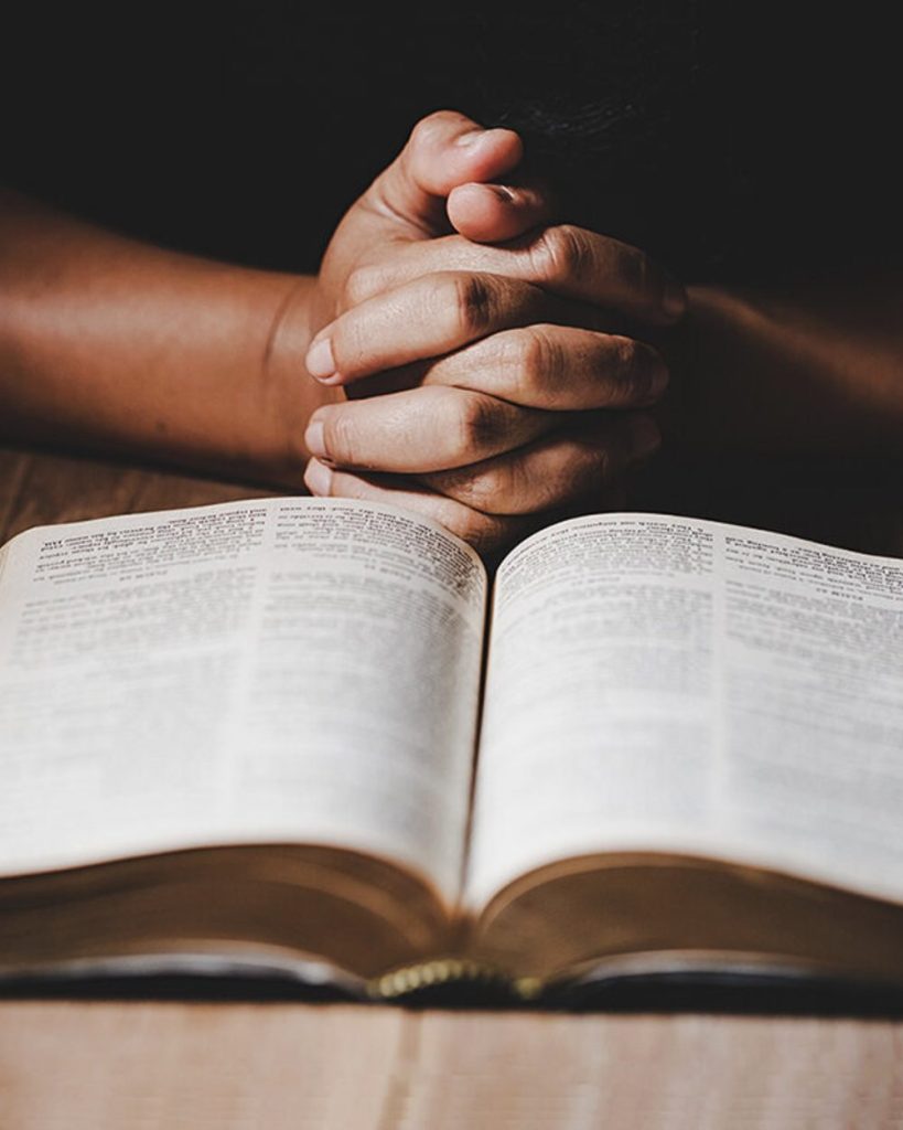 Hands folded in prayer over an open Bible